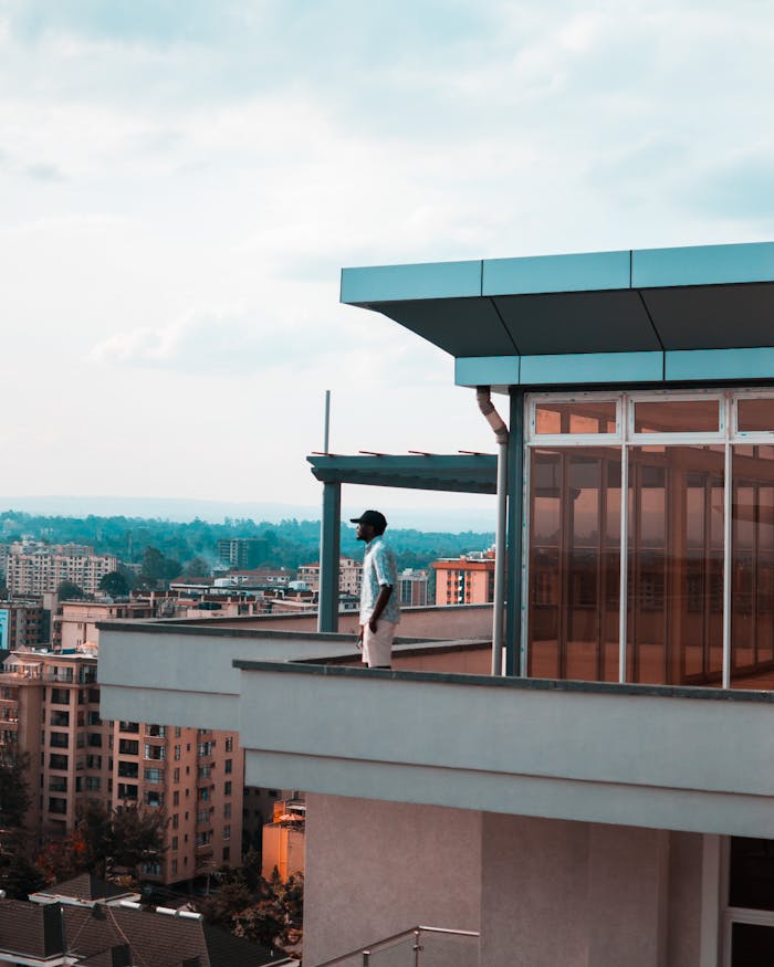 Hombre de pie en un balcón moderno con vistas al horizonte de la ciudad en un día brillante.